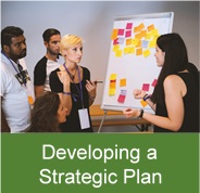 Click on this image of five people brainstroming with sticky notes to access information on developing a strategic plan.
