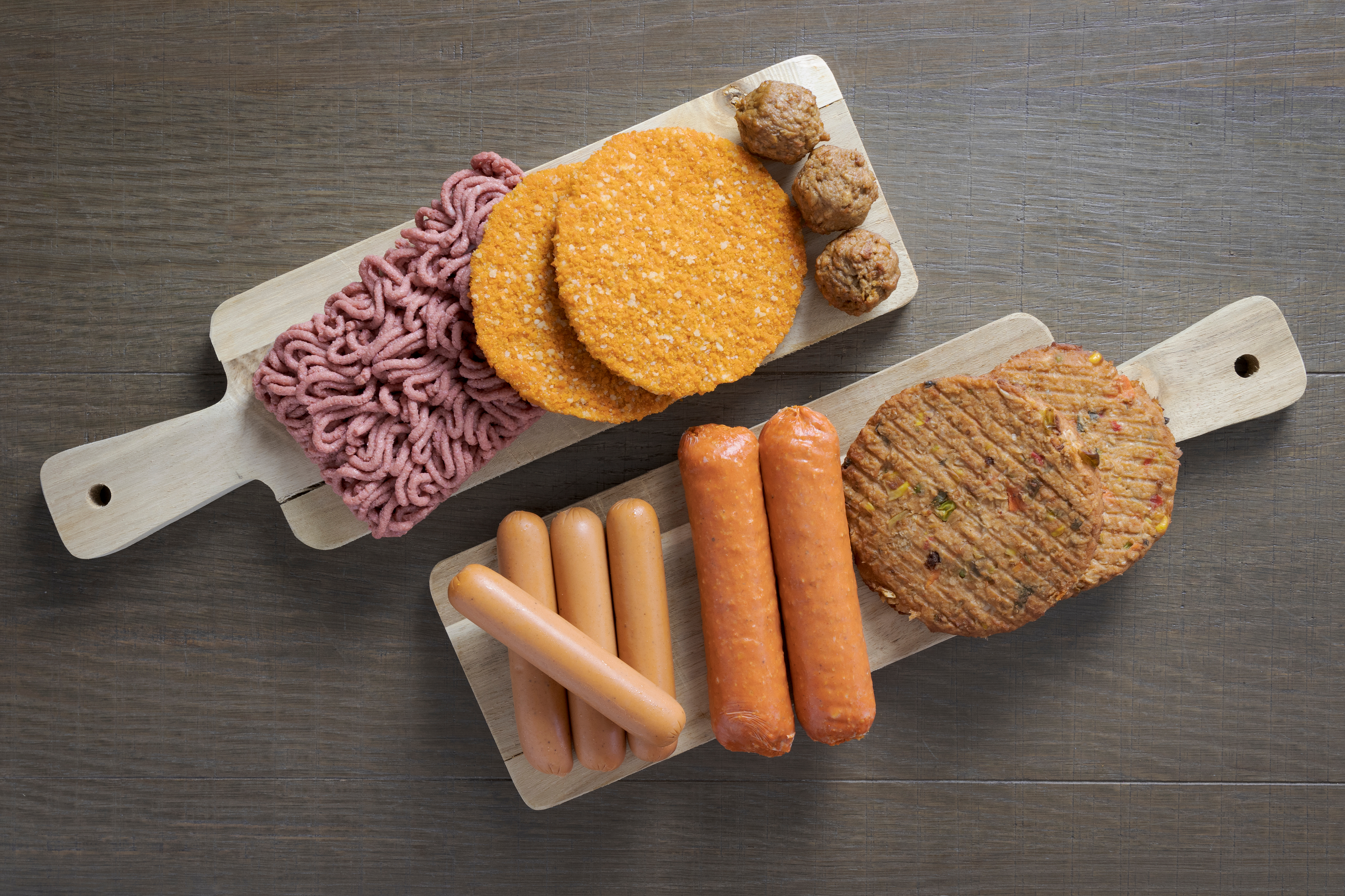 Photo of plant-based protein alternatives like veggie dogs and patties, and meatless meatballs arranged on serving paddles 