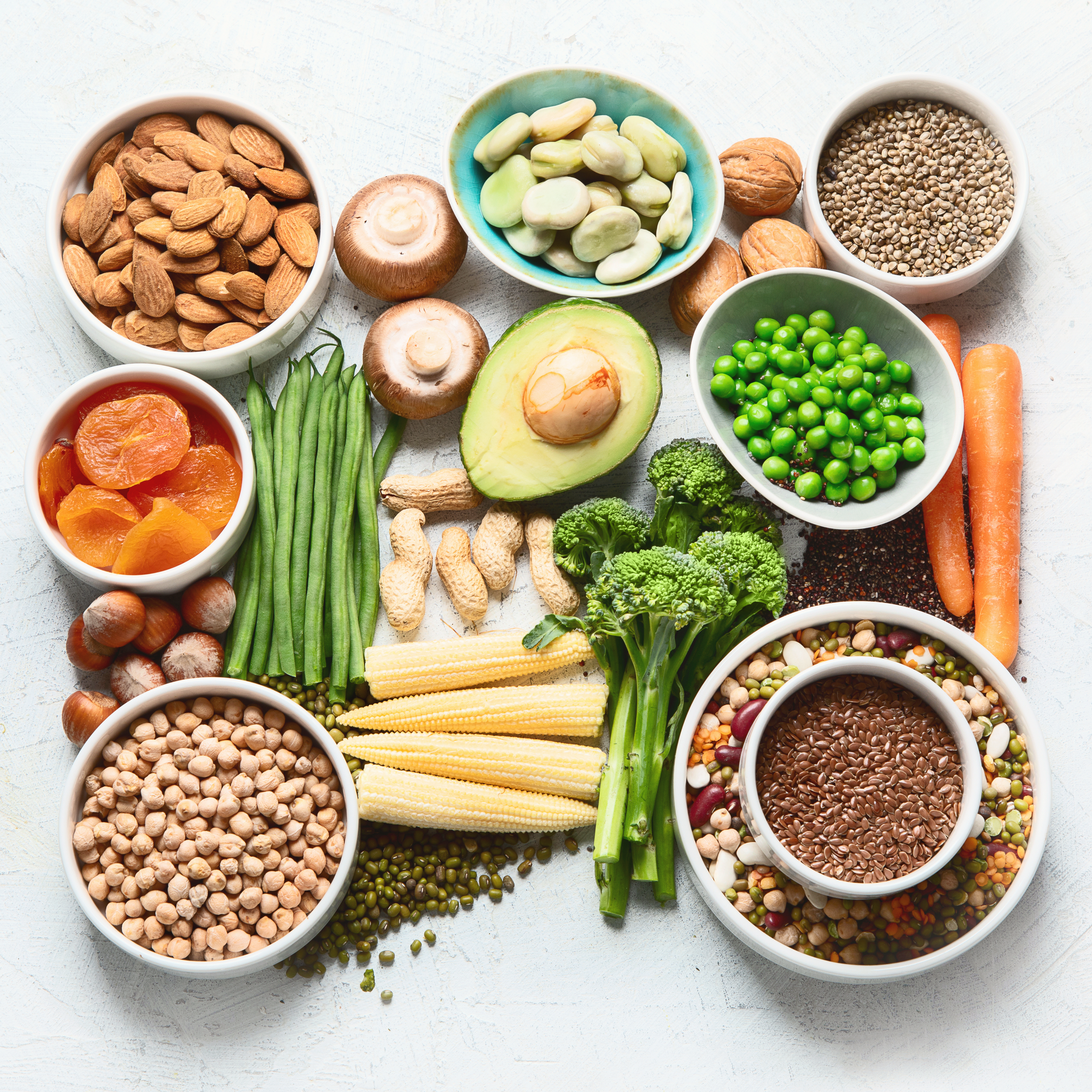 Photo of plant based proteins like legumes, pulses, nuts, and vegetables arranged on a white backdrop