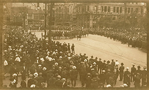 Une rue de Winnipeg en 1919. Une foule nombreuse se tient de chaque côté de la rue. Deux rangées de policiers à cheval défilent au milieu de la rue.