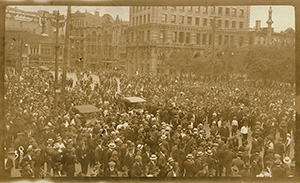 Une foule nombreuse se tient dans la rue à Winnipeg en 1919. Deux automobiles se trouvent au milieu de la foule. Des bâtiments bordent la rue en arrière-plan.