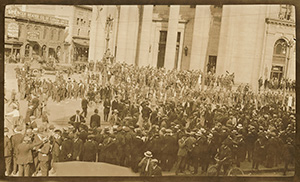 Une grande foule de personnes se tenant au milieu de l'avenue Portage et de la rue Main à Winnipeg, 1919. Un bâtiment à l'arrière-plan indique : Spencer Heater Co of Canada Ltd. Spencer Self-Feed Steam and Hot Water Boilers. Western Gem Coal.