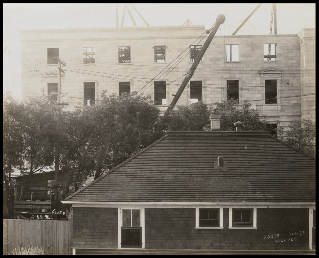 Photo of a house adjacent to the constuction, with a crane and an almost complete wall in the background.