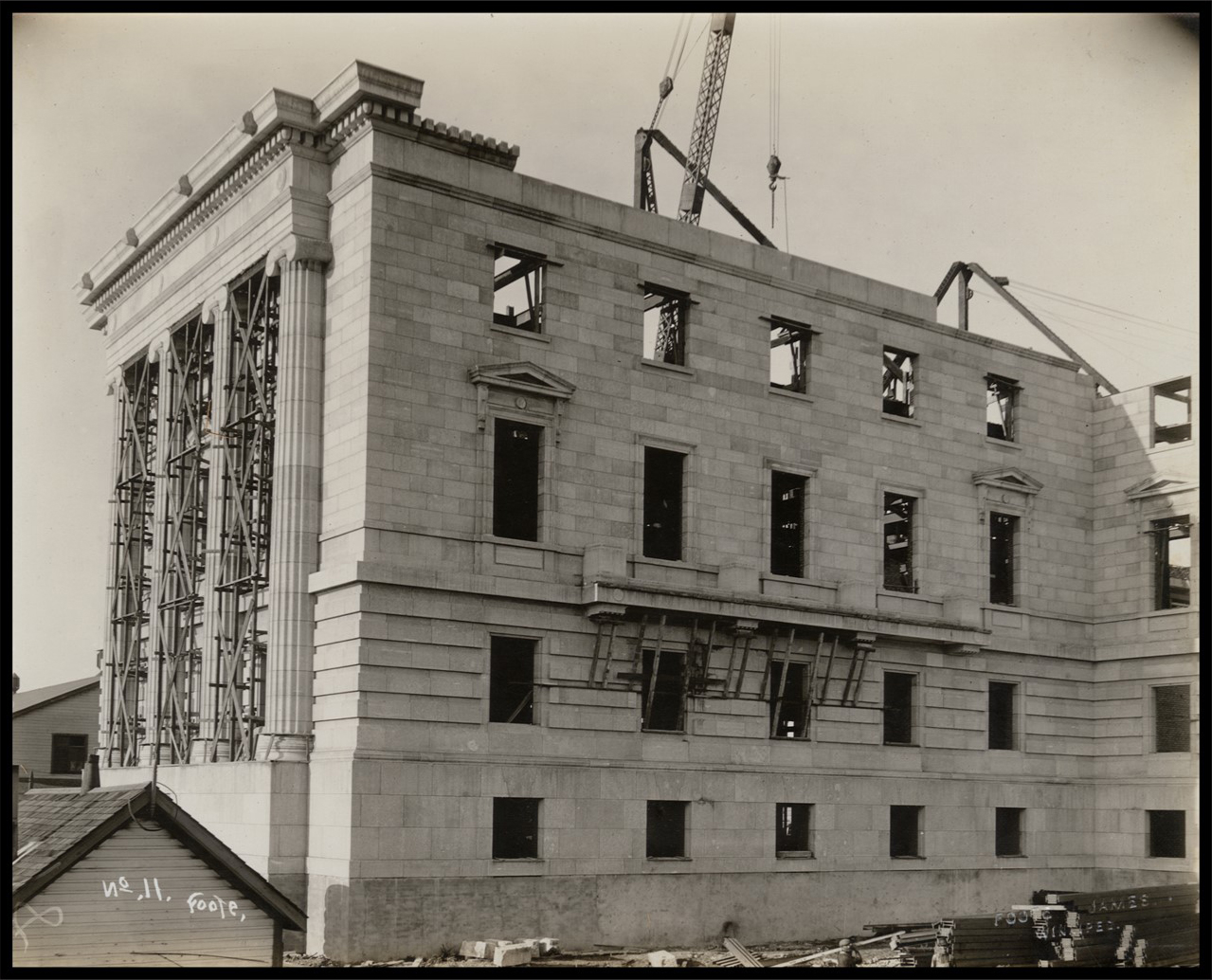 Photo of the exterior of the southeast part of the building. The walls are almost complete, but there is no roof nor windows. There is scaffolding in between the stone columns.