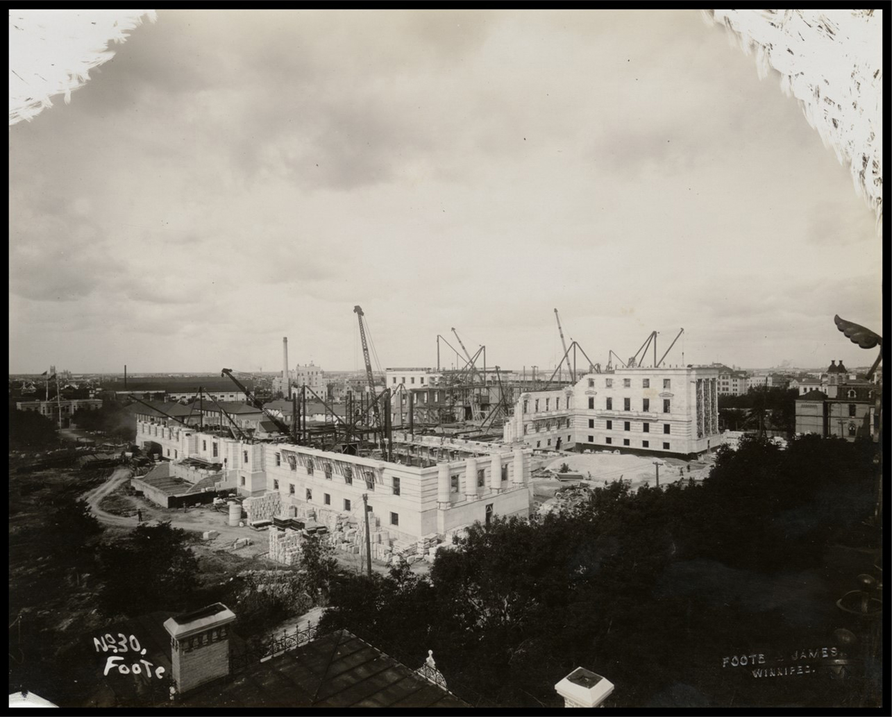 Wide aerial view of the Legislative Building under construction. Some walls are complete, while others are still being created. There are cranes inside the building and no roof.