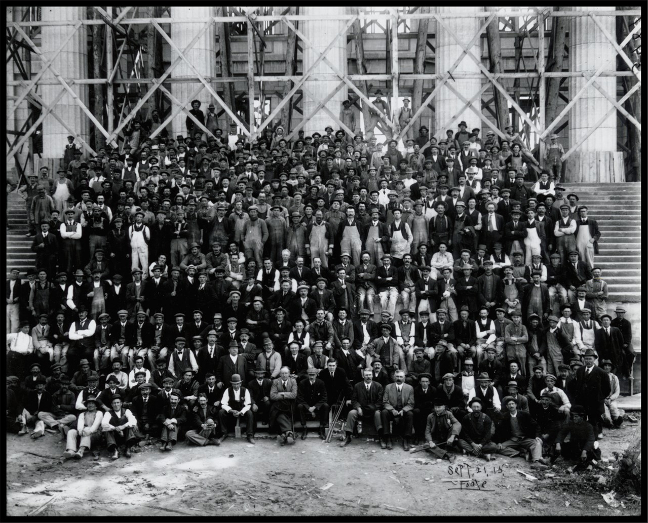 Photo of hundreds of men involved in the construction of the Legislative Building. They are standing or sitting on the steps of the building, which is still under construction.