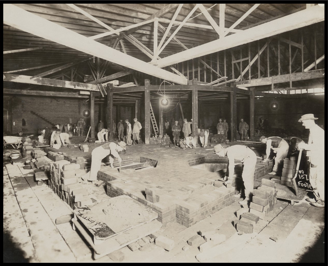 Interior photo of what will become the Rotunda, with several men laying bricks on the floor.