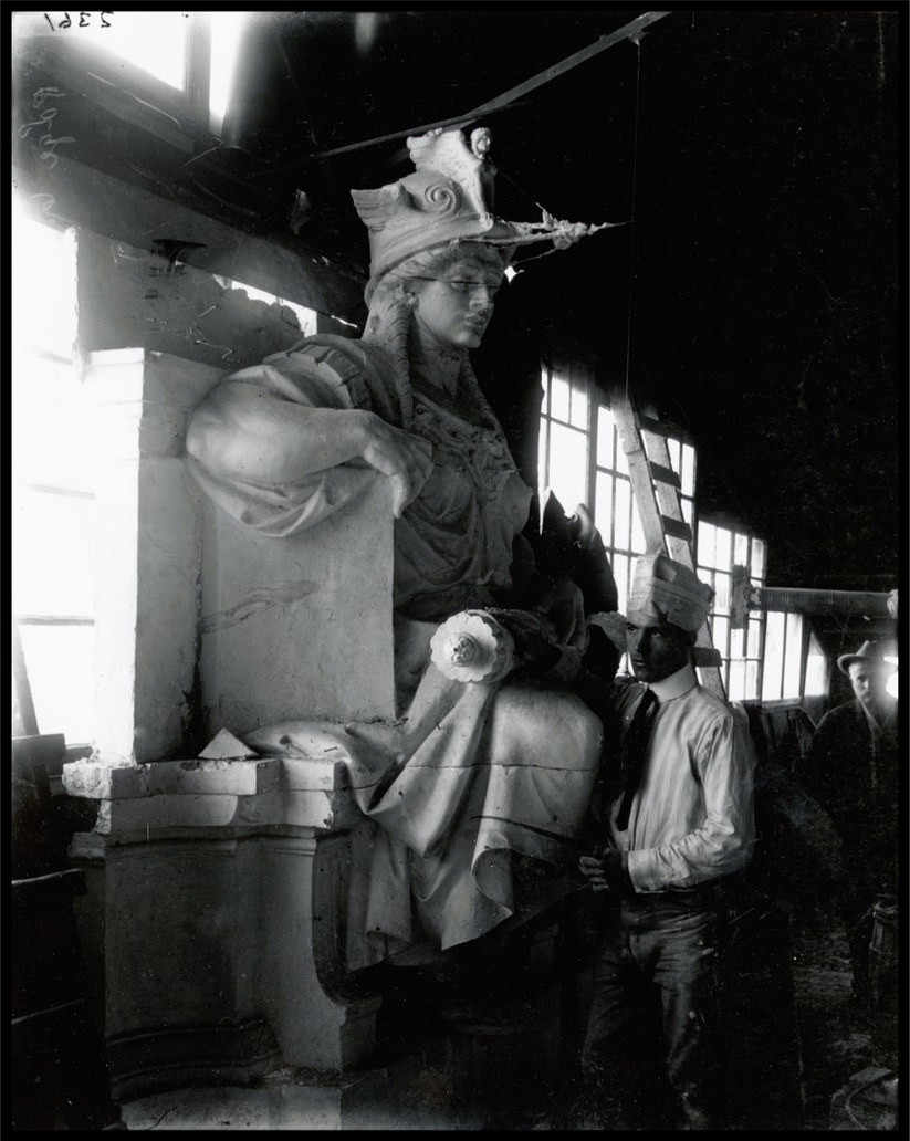 Photo of a man standing next to a giant carved sculpture resembling a woman.