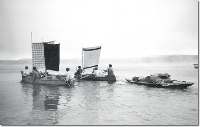 photo of men in canoes that are using point blankets as sails