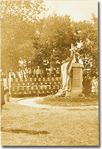 Photo of the unveiling of the 44th Battalion Memorial in 1926. A group of military personnel, dignitaries, and civilians stand respectfully around a rectangular monument with a cross on the top. A long cloth is draped around the Memorial.