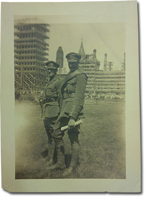 two men smiling and standing in uniform in front of buildings which are covered in construction scaffolding