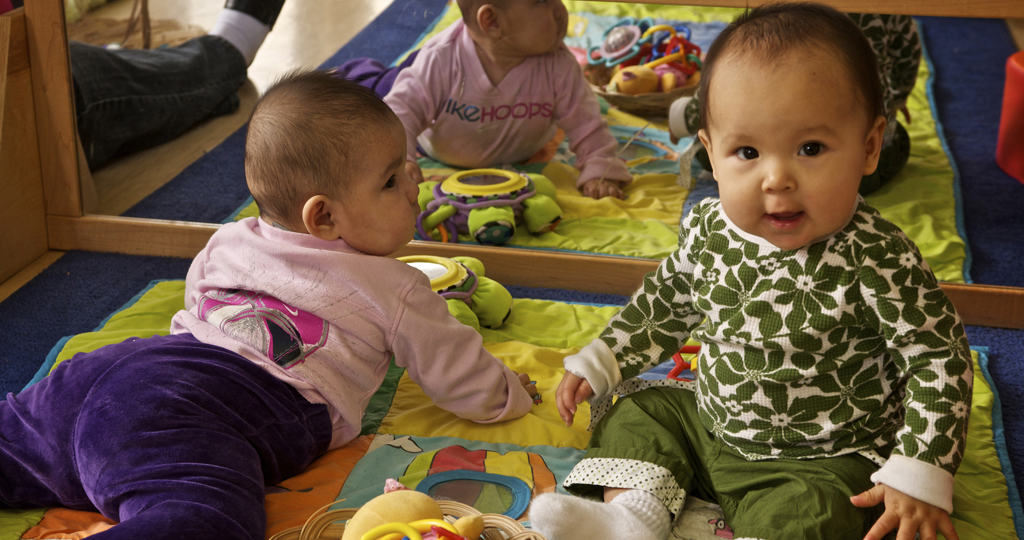 Two babies sitting in front of a mirror smiling