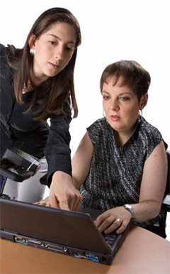 woman typing on a lap top and another woman pointing to the screen