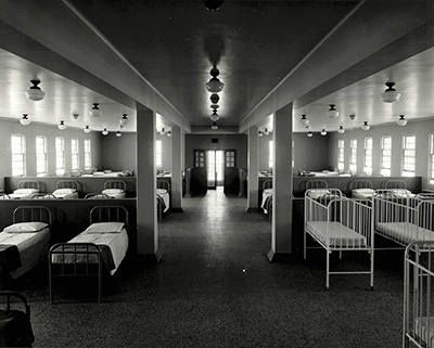 rows of empty beds and cribs in an institutional ward
